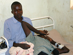 Distraught young man sitting in bed next to his comatose brother in a rural health center.
